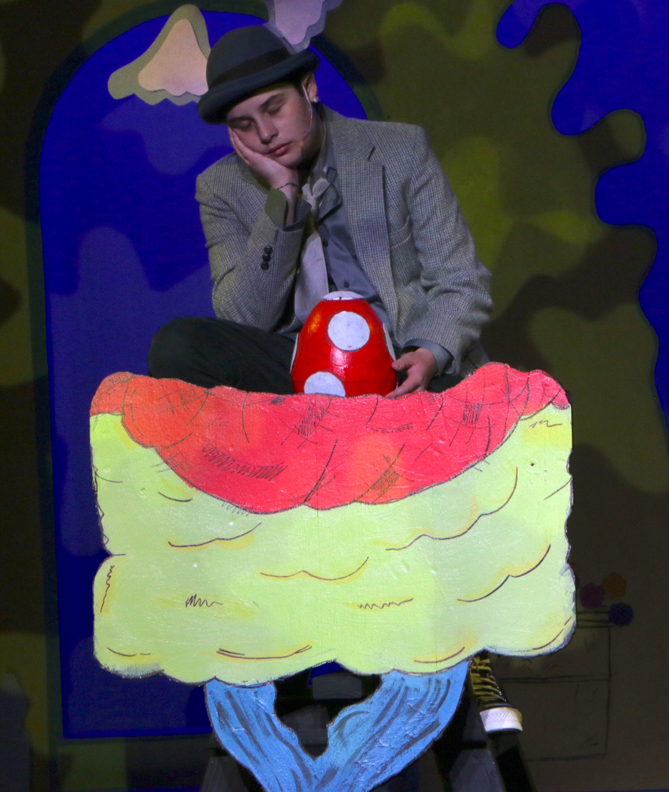 Student performing on stage - boy with a hat looking down at a red egg with white spots