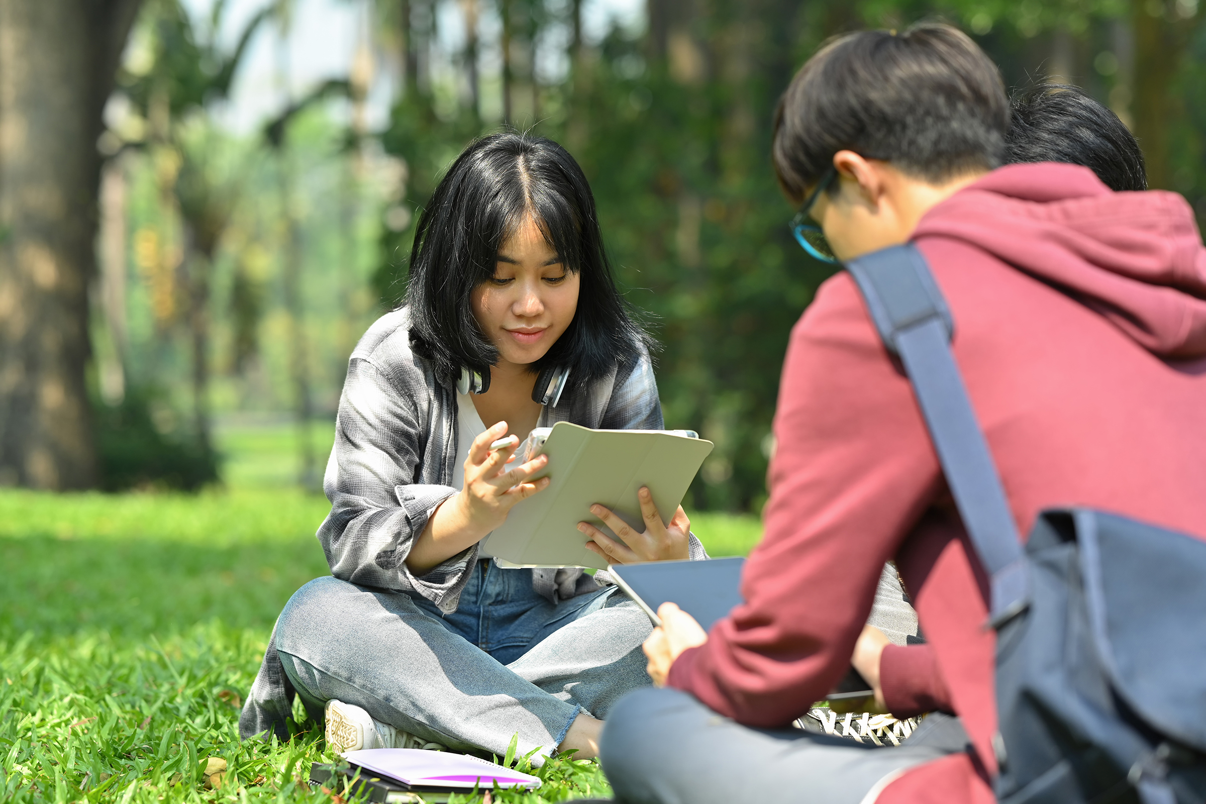 Image of a female student reading books with her friends at summer park.