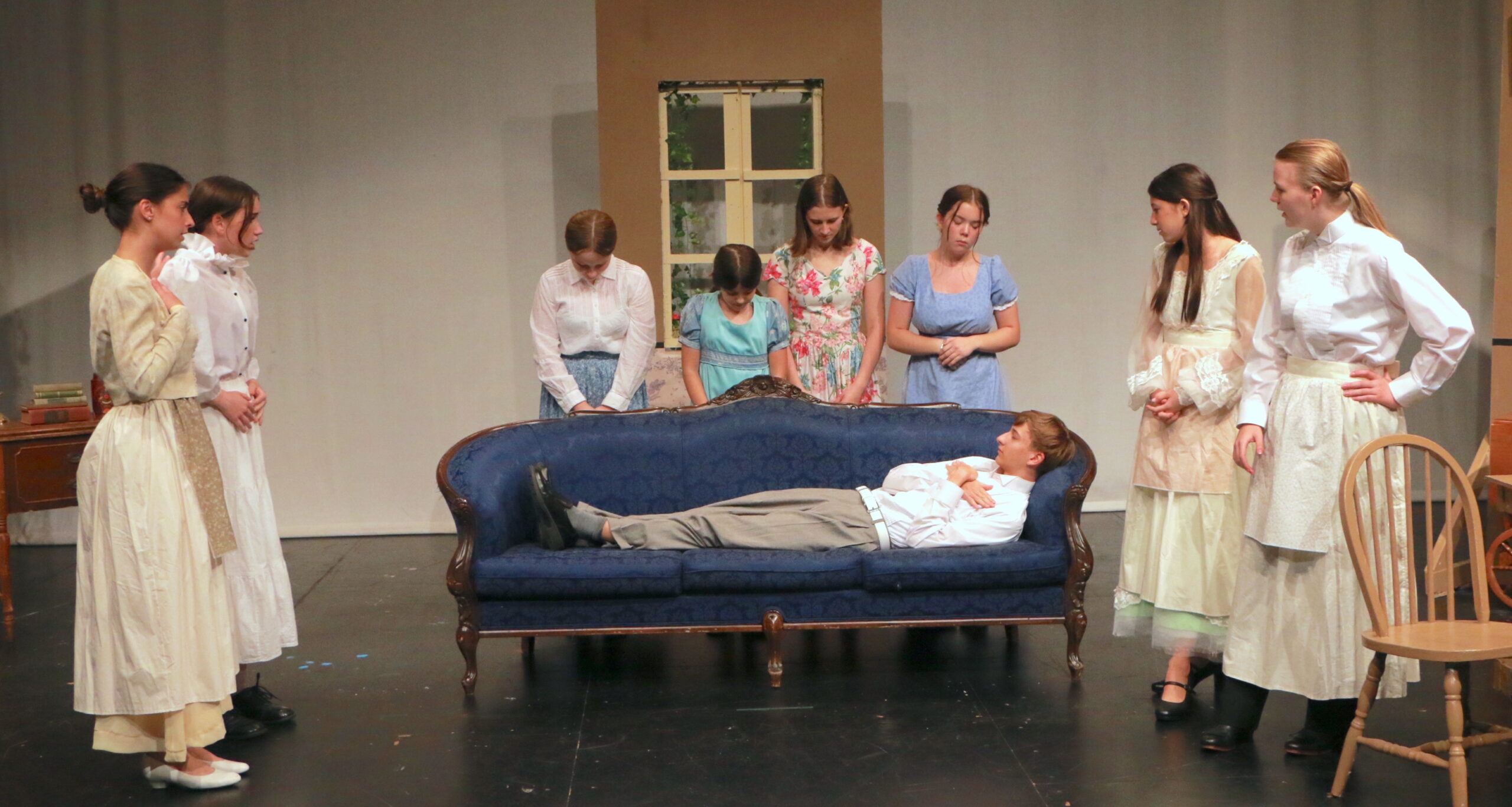 Man laying on the couch, while four people are standing behind the couch looking down at him